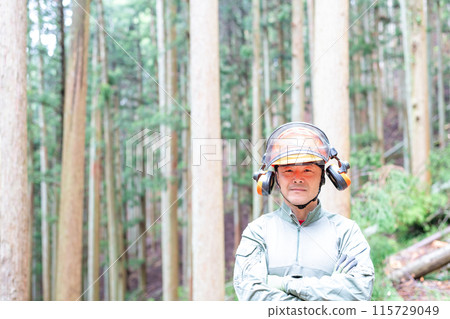 A forest worker with his arms folded, with the mountain forest in the background at his workplace A forest worker with his arms folded, with the mountain forest in the background at his workplace 115729049