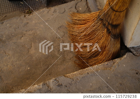 A broom made of natural materials, knitted from dry plant branches, stands against the wall next to the stairs 115729238