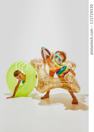 Little children, boy and girl in swimwear and diving masks have fun with pool floats ready to swim against white studio background. 115729330