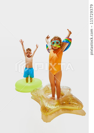 Little children, boy and girl in swimwear and diving masks have fun with pool floats against white studio background. Little children, boy and girl in swimwear and diving masks have fun with pool floats against white studio background. 115729379