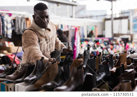 Rdinary african american guy chooses shoes at a flea market Rdinary african american guy chooses shoes at a flea market 115730531