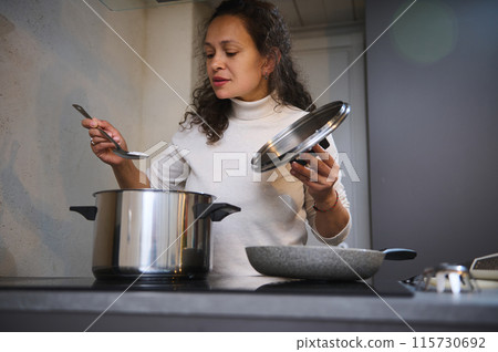 Woman cooking soup in modern kitchen with large pot Woman cooking soup in modern kitchen with large pot 115730692