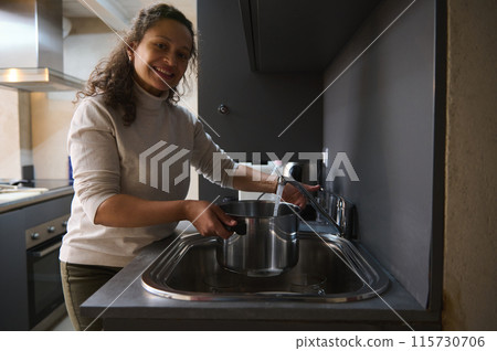 Woman happily filling pot with water in modern kitchen 115730706