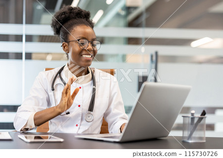 A smiling doctor wearing a stethoscope holding a virtual consultation with a patient on a laptop in a modern office. A smiling doctor wearing a stethoscope holding a virtual consultation with a patient on a laptop in a modern office. 115730726