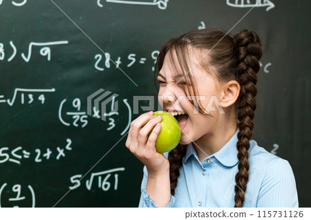 Teen girl funny emotionally bites a green apple at school Teen girl funny emotionally bites a green apple at school 115731126
