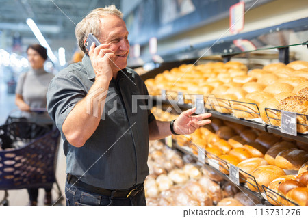 Elderly man consulting on mobile phone while shopping at grocery store 115731276
