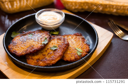 Fried grated potato pancakes with sour cream on frying pan 115731291