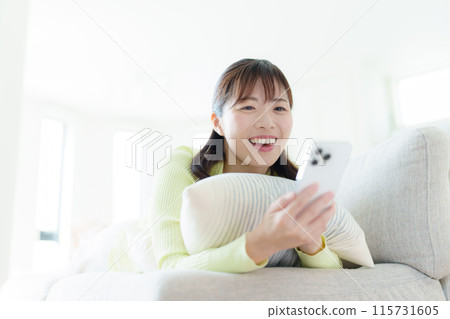 一名年輕女子躺著，拿著智慧型手機 115731605