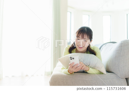 一名年輕女子躺著，拿著智慧型手機 115731606