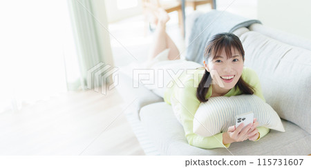 一名年輕女子躺著，拿著智慧型手機 115731607