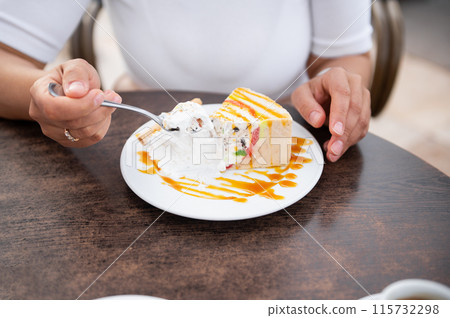 Person enjoying a delicious cream cake at a cafe table 115732298