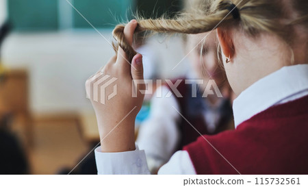 A girl touches a braid of her hair during class. 115732561