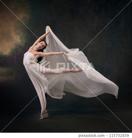 Dancer's graceful jump captured with her gown billowing like wings against vintage studio background. 115732839