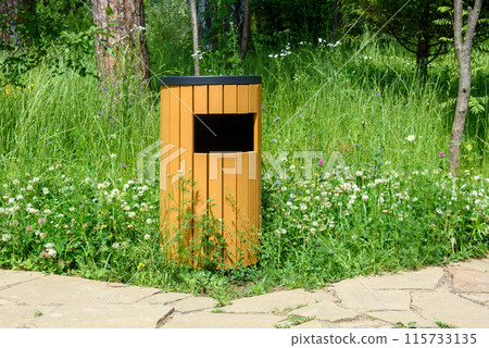 A wooden trash can sits next to a winding stone path in a  park. 115733135
