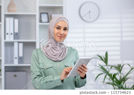 Confident Muslim woman in a modern office setting, using a digital tablet to perform business tasks. Professional and tech-savvy. Confident Muslim woman in a modern office setting, using a digital tablet to perform business tasks. Professional and tech-savvy. 115734623