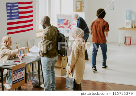 High angle view wide shot of diverse citizens taking ballot papers and voting at polling station on election day, copy space 115735379