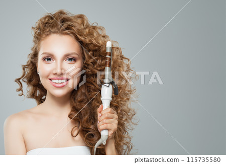 Pretty young smiling woman holding using hot curling tongs iron on white background.  115735580