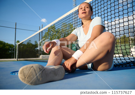 Female tennis player resting on court after match Female tennis player resting on court after match 115737627