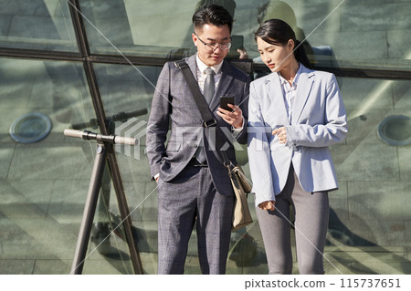 young asian businessman and businesswoman looking at cellphone together outdoors young asian businessman and businesswoman looking at cellphone together outdoors 115737651
