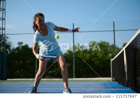 Woman playing tennis on court during sunny day 115737847