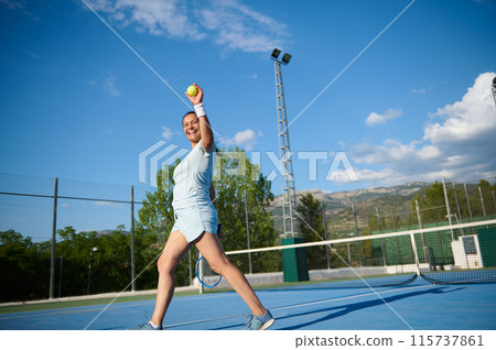 Happy woman playing tennis on outdoor court under blue sky 115737861