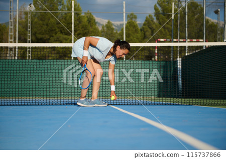 Female tennis player picking up ball near net on court Female tennis player picking up ball near net on court 115737866