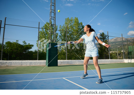 Young woman playing tennis on an outdoor court on a sunny day 115737905
