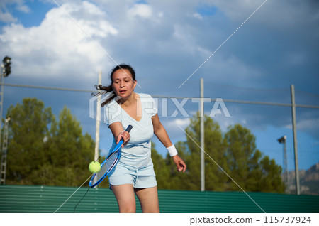 Woman playing tennis on an outdoor court under a cloudy sky Woman playing tennis on an outdoor court under a cloudy sky 115737924