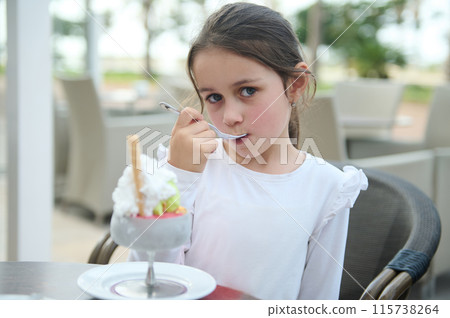 Little girl enjoying ice cream sundae at outdoor cafe 115738264