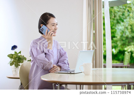 A middle-aged woman looking at a computer while using her smartphone in the living room A middle-aged woman looking at a computer while using her smartphone in the living room 115738974