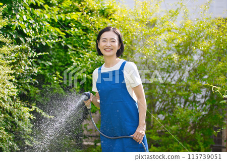 微笑的中年婦女在花園裡的綠樹澆水 微笑的中年婦女在花園裡的綠樹澆水 115739051
