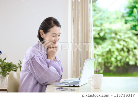 中年婦女在客廳喝咖啡時看著電腦 中年婦女在客廳喝咖啡時看著電腦 115739317