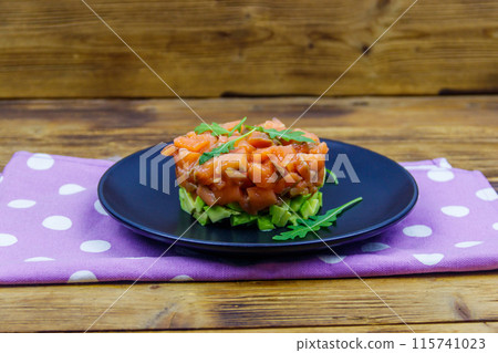 Salmon tartare with avocado and arugula on wooden table 115741023