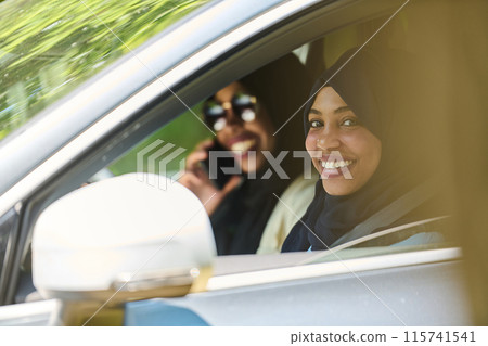 Two Muslim women wearing hijab converse on a smartphone while traveling together in a car through the  115741541