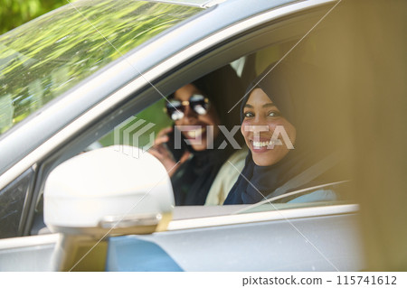 Two Muslim women wearing hijab converse on a smartphone while traveling together in a car through the  115741612