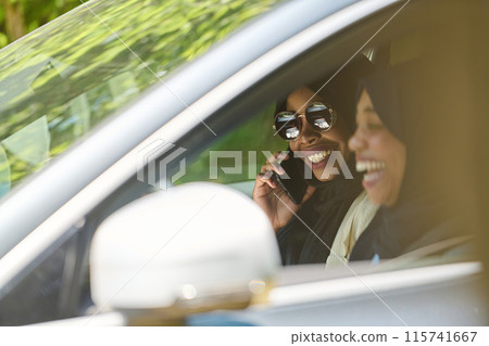 Two Muslim women wearing hijab converse on a smartphone while traveling together in a car through the Two Muslim women wearing hijab converse on a smartphone while traveling together in a car through the 115741667