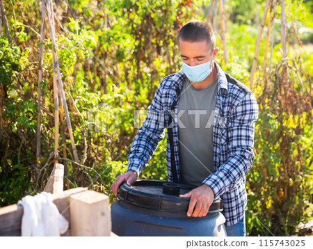 Male worker in mask arranging garden barrel 115743025