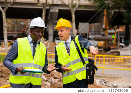 Engineer and architect are discussing options for laying a pipe on street Engineer and architect are discussing options for laying a pipe on street 115743066