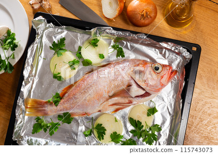 There is carcass of raw fish sea bass with spices on foil. 115743073
