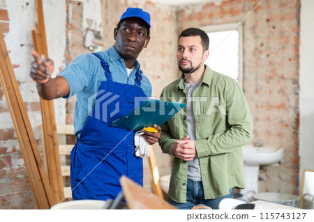 Worker and owner building discuss construction plan inside building under construction 115743127