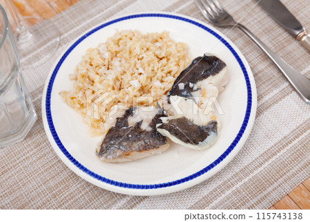 Tender meat of baked cod fillet is garnished with boiled basmati rice. 115743138