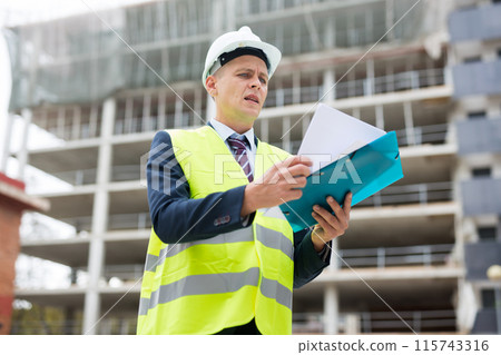 Architect standing on building site with documentation 115743316