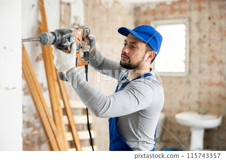 Professional builder drills a wall with a hammer drill Professional builder drills a wall with a hammer drill 115743357