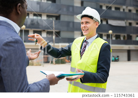 Engineer giving keys to new apartment to man 115743361