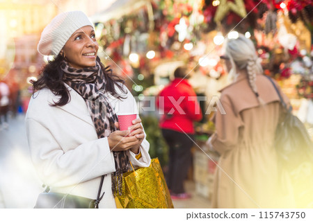 Happy woman holding cup of coffee in hands at street christmas fair 115743750