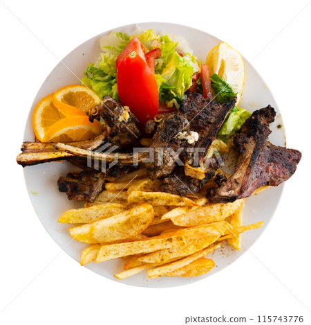 Delicious browned grilled lamb ribs served with crispy french fries and lettuce with tomato on plate, decorated with lemon 115743776