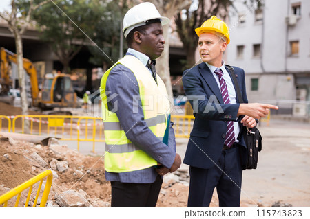 Engineer and architect are discussing options for laying a pipe on street Engineer and architect are discussing options for laying a pipe on street 115743823