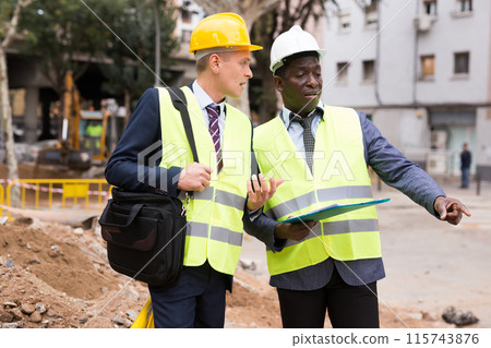 Two men workers discuss the project, holding work documents Two men workers discuss the project, holding work documents 115743876