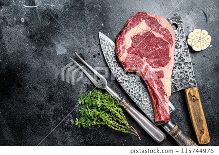Dry aged raw tomahawk or cowboy beef steak on a black table with knife, cleaver, spice and herbs. Black background. Top view. Copy space Dry aged raw tomahawk or cowboy beef steak on a black table with knife, cleaver, spice and herbs. Black background. Top view. Copy space 115744976