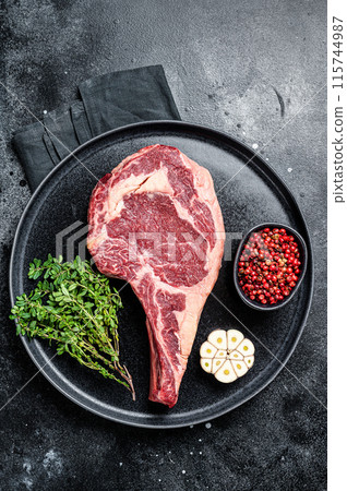 Dry aged cowboy or rib eye steak, raw beef meat with herbs. Black background. Top view 115744987